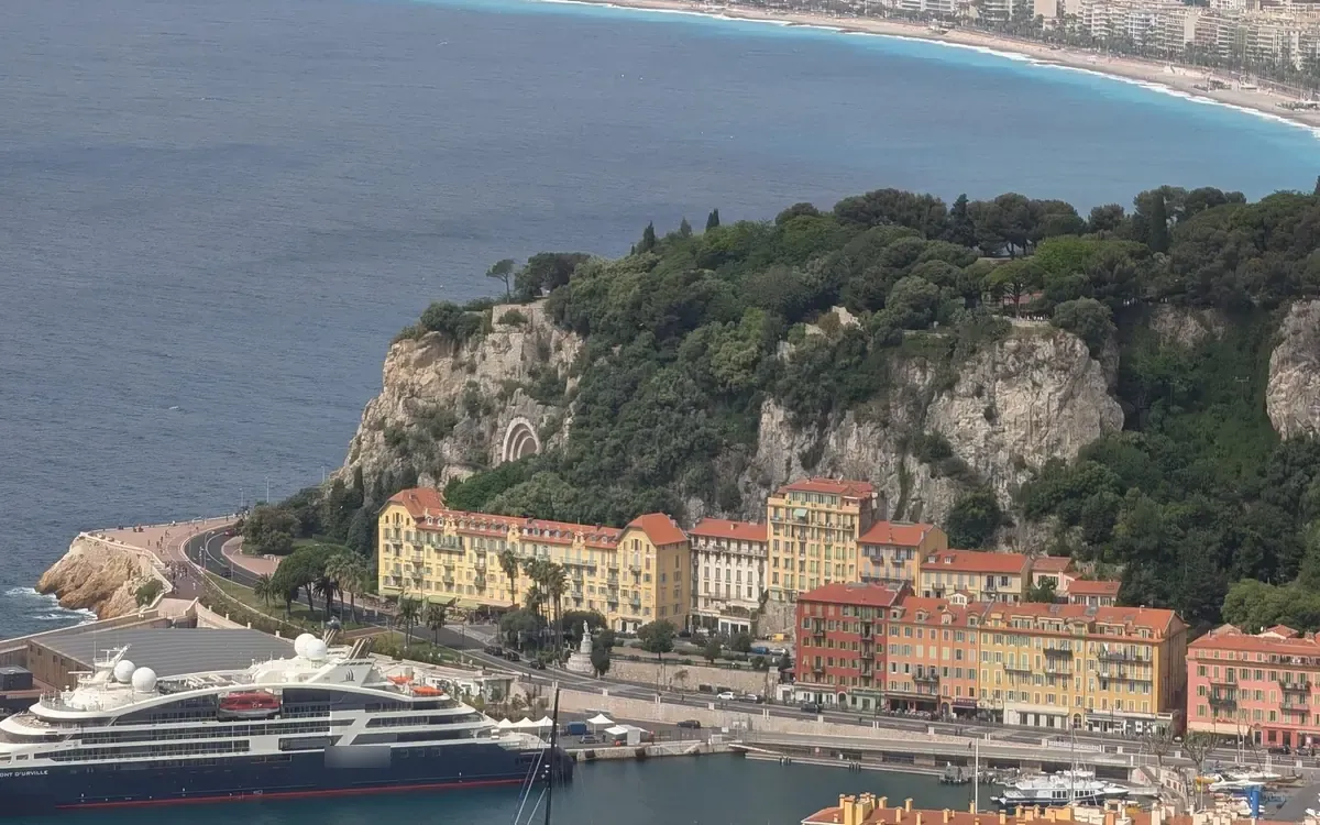 Nice harbour from above: a cruise ship at the quay below yellow and terracotta buildings, the bay curving away behind