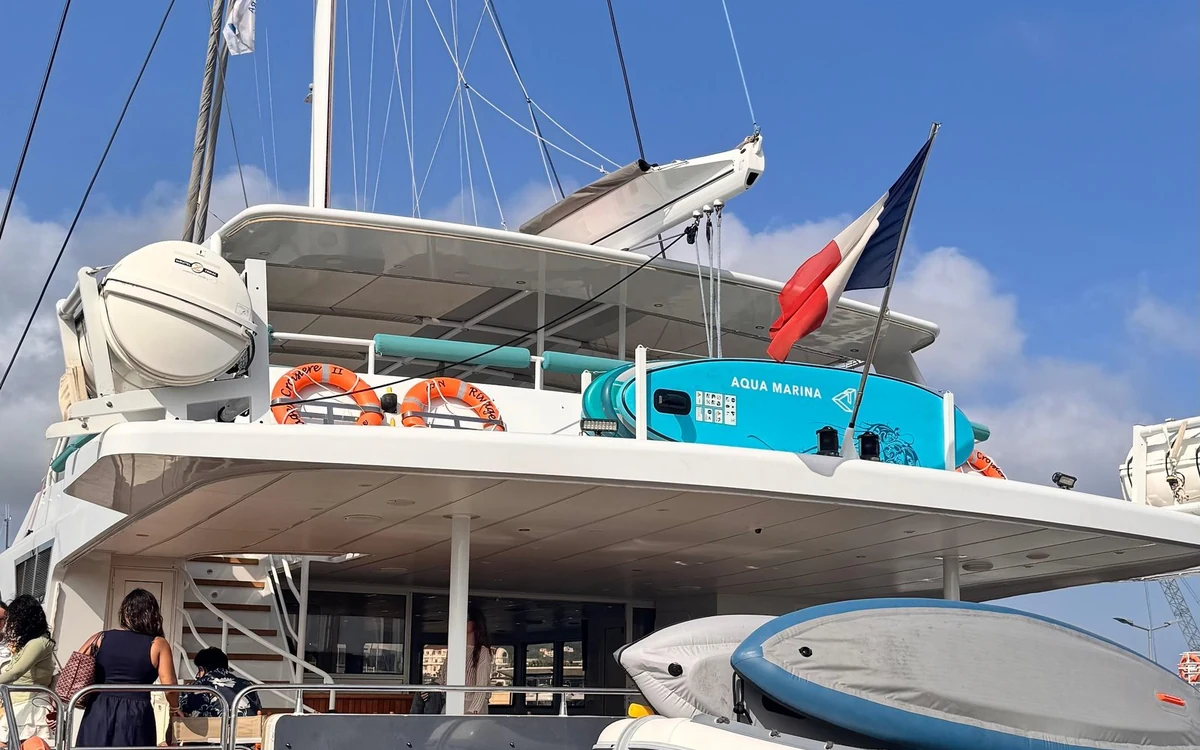 The stern of a large catamaran with paddle boards, lifebuoys and a French flag