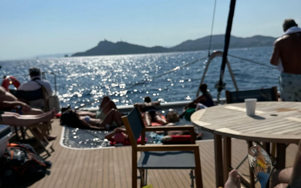 People stretched out in the sun on a catamaran deck, hills on the horizon