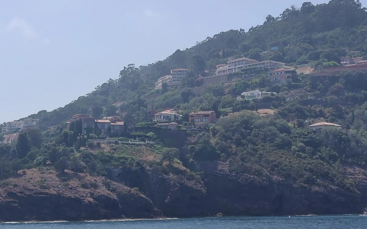 Wooded hills with villas above a rocky shore, seen from the water