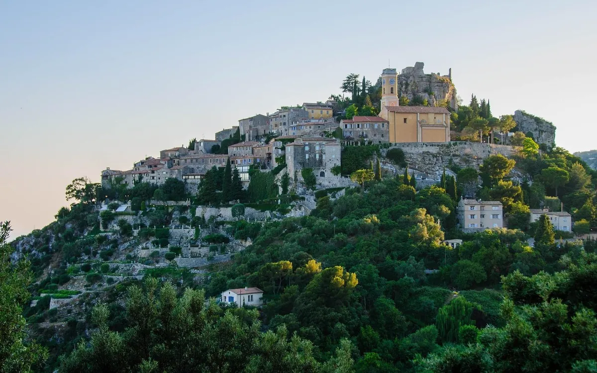 Èze: stone houses and a church tower on a wooded hilltop in the evening light