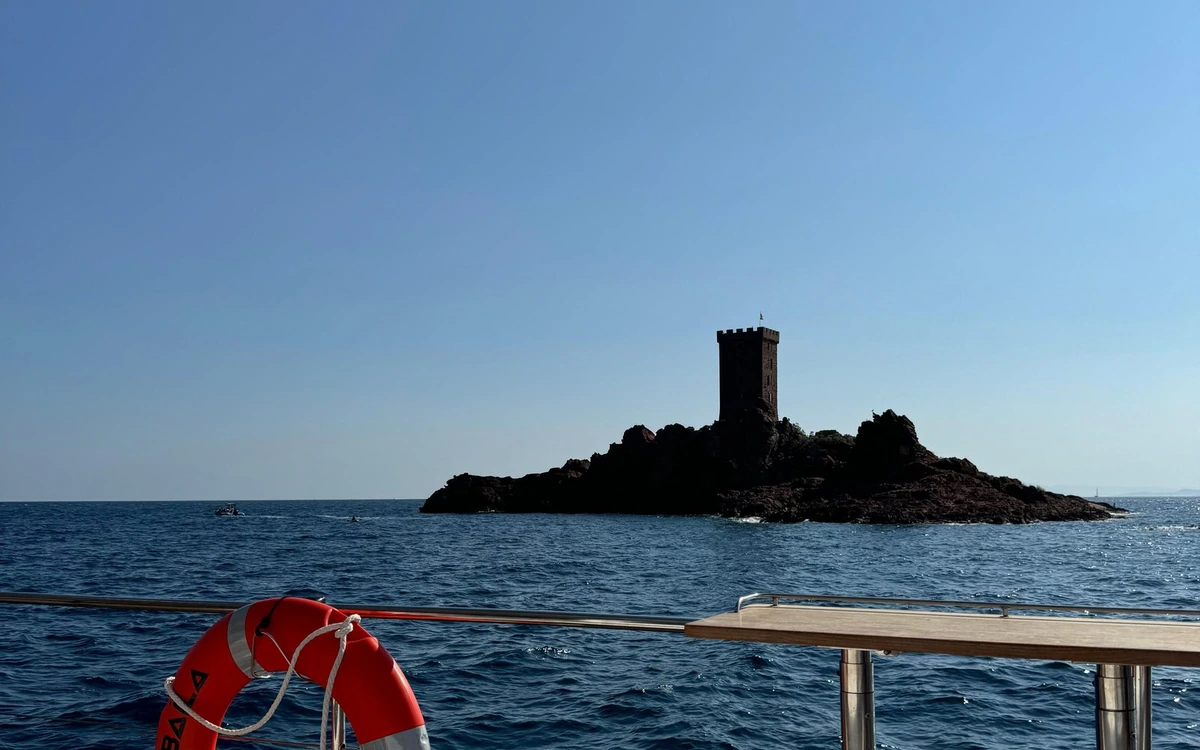 A rocky islet with a square stone tower, seen from the rail of a boat