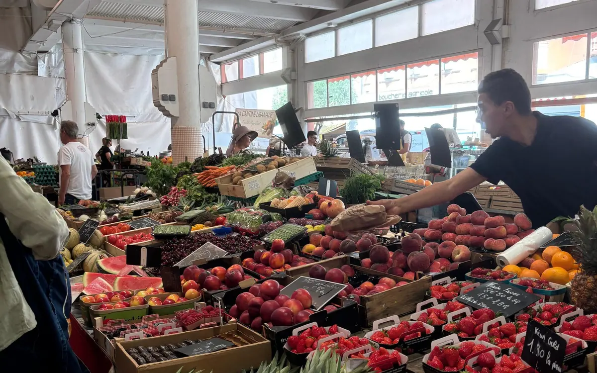 Crates of peaches, strawberries, melons and oranges on a market stall under a covered roof