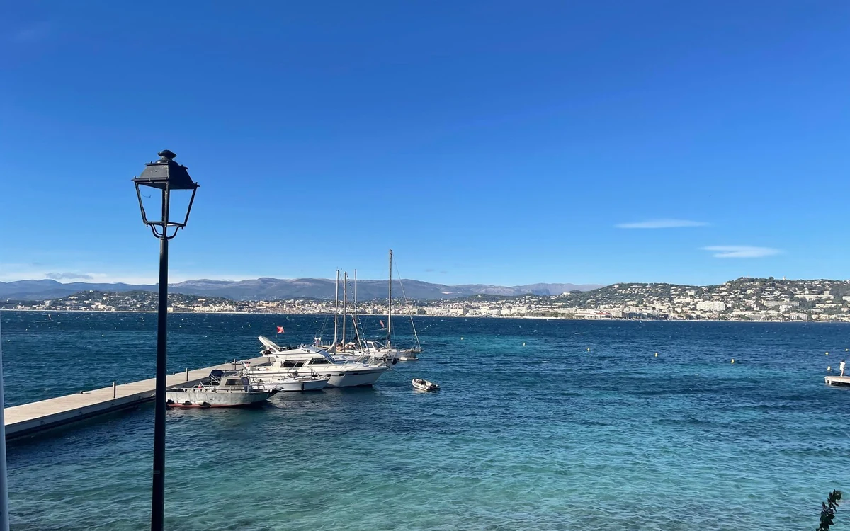 Boats moored at a pier on Île Sainte-Marguerite, with Cannes and the hills across the water