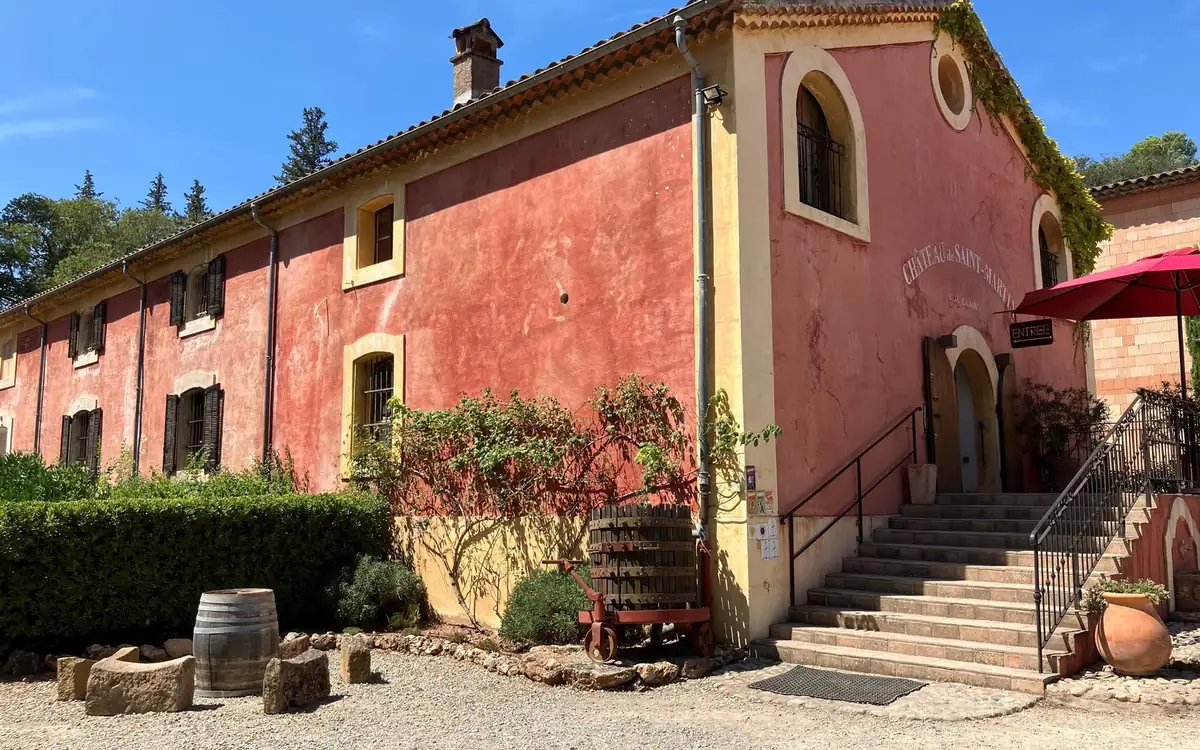 A pink-walled wine estate with green shutters, stone steps and an old barrel by the door