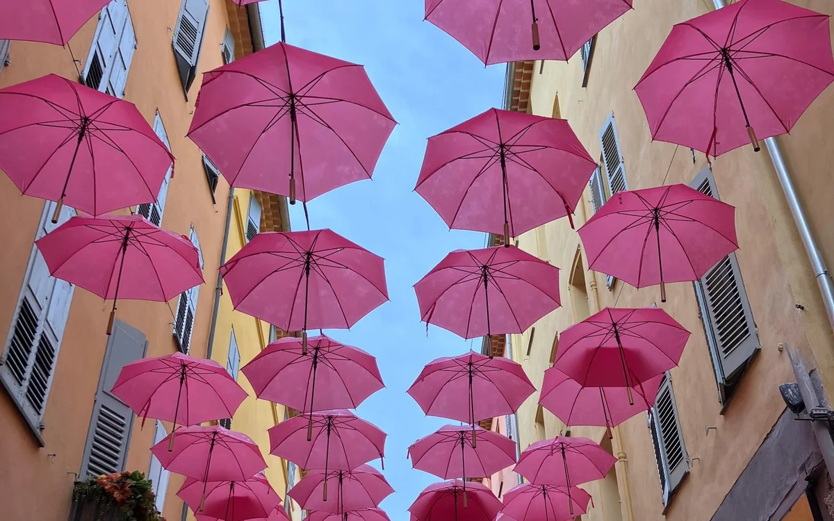 Pink umbrellas hung in rows over a narrow village lane