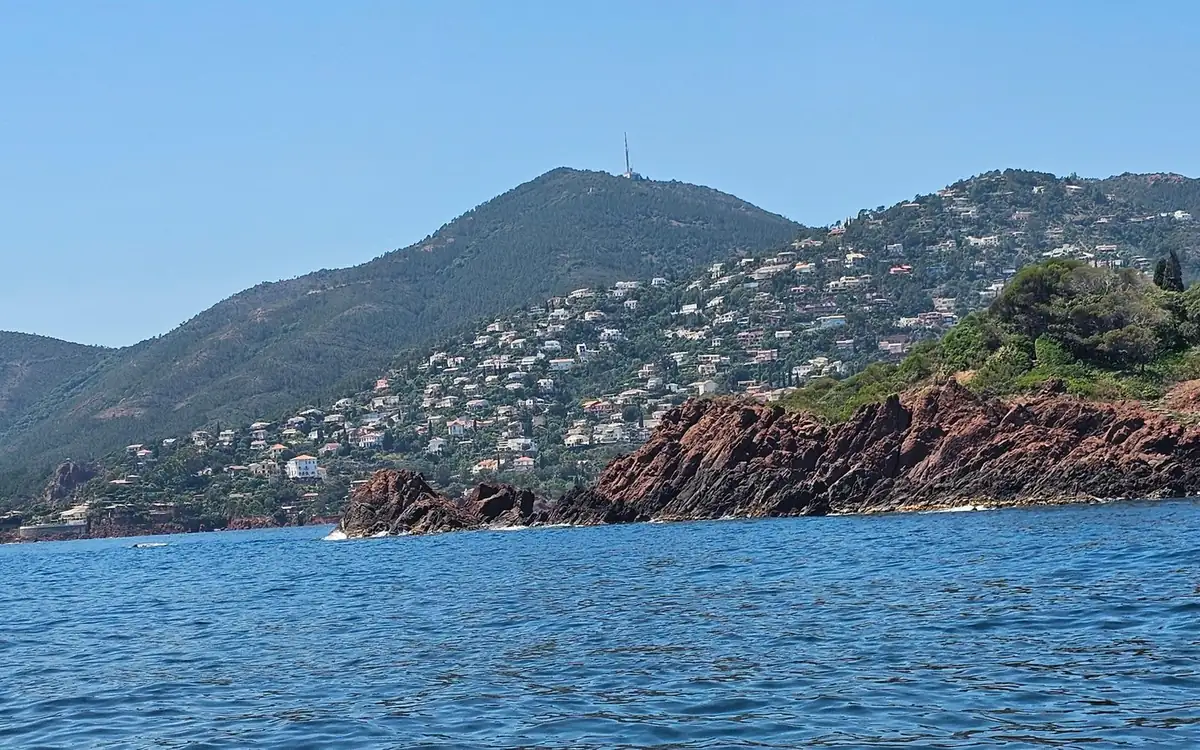Red rocks at the water's edge below green hills dotted with houses