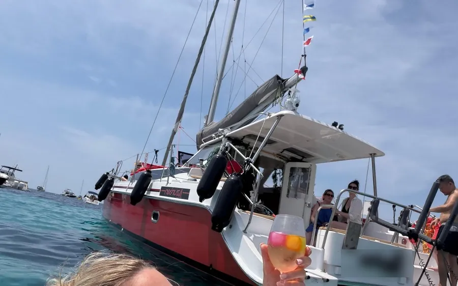 A red-hulled catamaran moored in turquoise water, a guest raising a drink