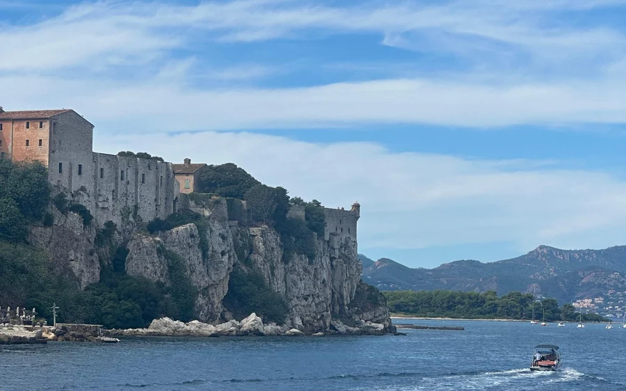 Old stone fortifications on a cliff above the sea, a motorboat passing below