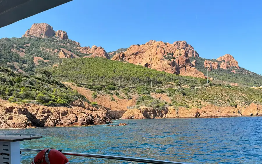 Red rock peaks and cliffs above the sea, seen from the deck of a boat