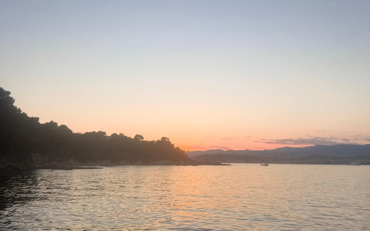 The sun going down behind a wooded headland, its light on still water