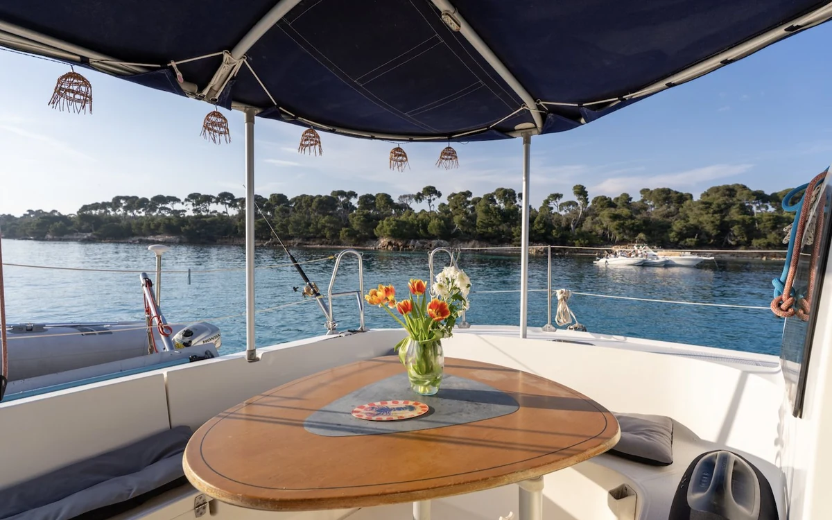 A table with flowers under the shade of a catamaran deck, the coast behind